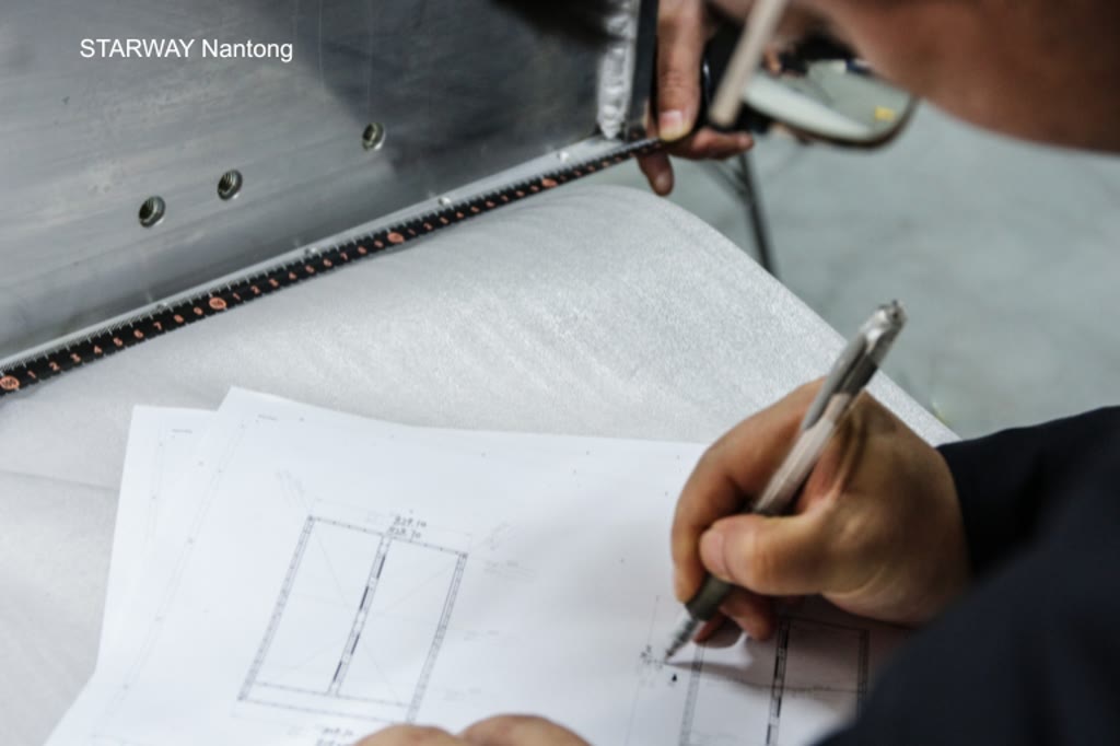 Engineer marking a correction on a customer technical drawing beside a sheet metal assembly